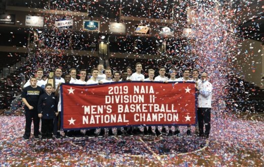 The men's basketball team poses amid confetti behind the NAIA National Champions banner